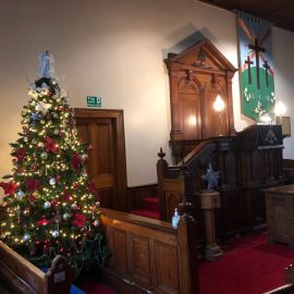 Christmas tree lit with fairy lights at the side of the pulpit in Legacurry church